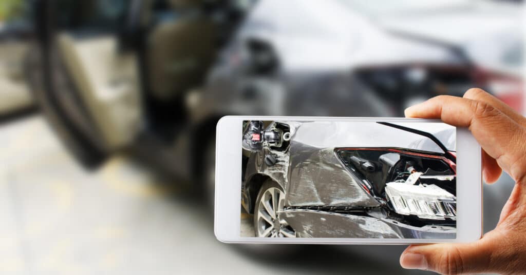 man taking picture of wrecked vehicle with phone